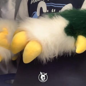 May include: A pair of furry hand paws with yellow claws. One paw is white with green and light green fur accents. The other paw is white with yellow claws.