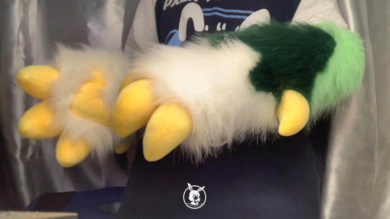 May include: A pair of furry hand paws with yellow claws. One paw is white with green and light green fur accents. The other paw is white with yellow claws.