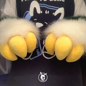 May include: A pair of furry green and white hand paws with yellow claws. The claws are made of soft, plush material.