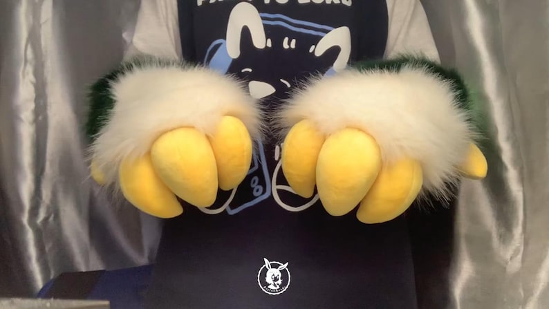 May include: A pair of furry green and white hand paws with yellow claws. The claws are made of soft, plush material.