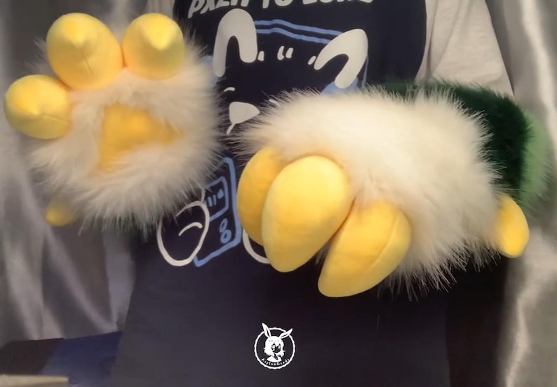 May include: A pair of furry hand puppets with yellow claws and white fur. The puppets are being worn by a person wearing a blue shirt with a graphic design.