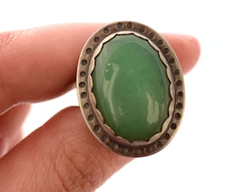 May include: A silver ring with a green oval gemstone set in a decorative border.