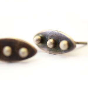 Abstract leaf stud earrings made with sterling silver. Three polished silver spheres soldered on top of the dark patina leaf shape. Perfect for everyday wear. On a white background.