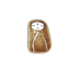 May include: A hand-painted stone with a simple white face and body, resembling a person. The stone is brown and has a rough texture.