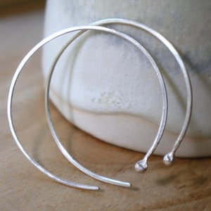 May include: A pair of silver hoop earrings with a hammered finish. The earrings are simple and elegant, and they would make a great gift for any occasion.
