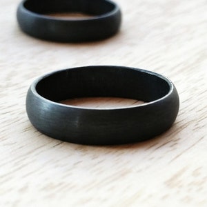 May include: Three black matte finish rings on a light wood surface.