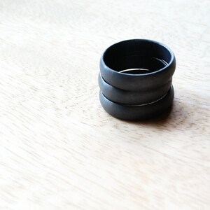 May include: Four black rings stacked on top of each other on a light wood surface.