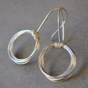 May include: A pair of silver wire earrings with a circular design. Each earring has multiple loops of wire that are twisted together to create a unique and modern look.