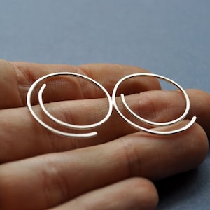 May include: A pair of silver-colored spiral earrings. Each earring features a continuous, curved design that forms a spiral shape. The earrings are shown against a neutral background, highlighting their minimalist and modern aesthetic. These earrings are a stylish accessory.