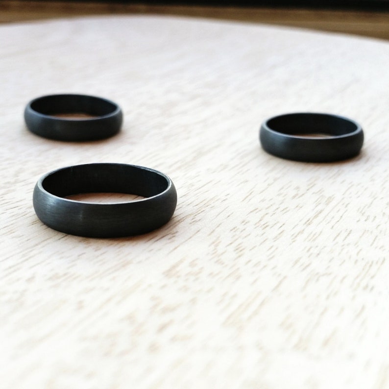 May include: Three black matte finish rings on a light wood surface.