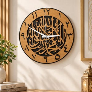 May include: A round wall clock featuring a light wood outer ring with black Arabic numerals and a black center panel displaying intricate gold-colored Arabic calligraphy. The clock has two white hands and a thin white second hand.