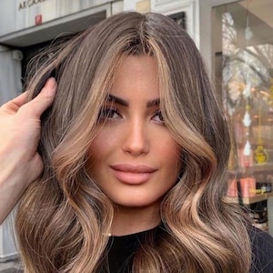 Pode incluir: Uma mulher com cabelo comprido, ondulado, castanho claro com luzes loiras. O cabelo está estilizado em ondas soltas e cai até os ombros.
