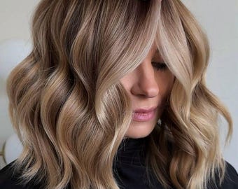 May include: A woman with long, wavy, light brown hair with blonde highlights. The hair is styled in a layered bob with a side parting.