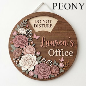 Puede incluir: Un letrero redondo de madera con un diseño floral y el texto "DO NOT DISTURB" y "Lauren's Office". El letrero presenta un borde de madera oscura, una sección de madera clara y una cuerda blanca para colgar. El arreglo floral incluye rosas rosas y blancas y pequeñas mariposas.