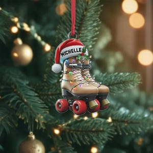 Könnte beinhalten: Ein Weihnachtsornament mit braunen Rollschuhen mit roten Rädern, gekrönt von einem Weihnachtsmütze mit dem Namen "Michelle". Die Rollschuhe sind mit einer Lichterkette geschmückt, die an einem roten Band hängt.