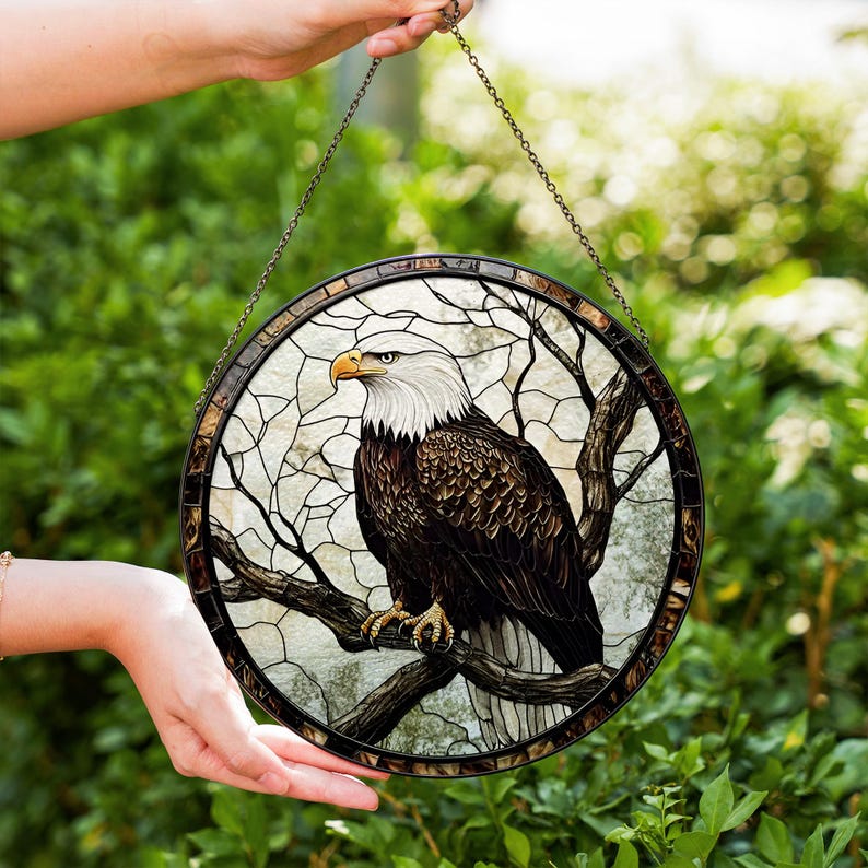 May include: Circular stained glass panel depicting a bald eagle on a tree branch. The eagle has a white head, brown body, and yellow beak. The panel is framed with a dark border and a chain for hanging. The background has a light, textured design.