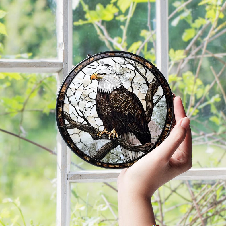 May include: Circular stained glass panel depicting a bald eagle on a branch. The eagle has a white head and yellow beak. The panel is framed in black with a mosaic border. The background is a light, abstract design. A decorative item.