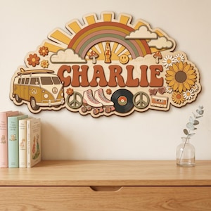 Puede incluir: Letrero de madera con el nombre "CHARLIE" en letras marrones, con un diseño retro con un arcoíris, sol, flores, una furgoneta, patines y un disco. El letrero es una pieza decorativa.