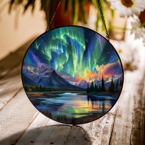 May include: A circular stained glass panel showcasing the aurora borealis above a mountain landscape and a tranquil lake. The artwork uses green, blue, purple, and orange hues, framed in black metal with a hanging chain. The scene captures the beauty of nature.