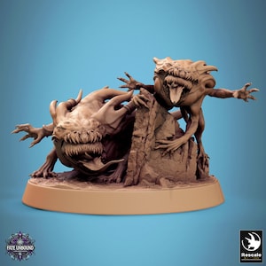 May include: A tan-coloured miniature sculpture depicting two monstrous creatures with sharp teeth and outstretched limbs. One creature is perched on a rocky formation. The base of the sculpture is light brown. The text "FATE UNBOUND" is visible.