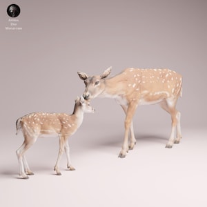 Pode incluir: Um par de figuras de veados. Um veado adulto e um filhote são retratados em marrom claro com manchas brancas. O veado adulto está encostando no filhote. As figuras são colocadas em um fundo macio e neutro.