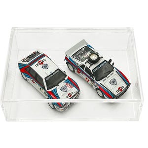 May include: Two white, blue and red toy cars in a clear acrylic display case. The cars are both Lancia 037s, one with the number 17 and the other with the Martini Racing logo.