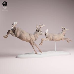 Puede incluir: Una escultura de dos ciervos en pleno salto, uno con cuernos, sobre una base blanca. Los ciervos son de color beige claro, con musculatura detallada. La escultura está sobre un fondo suave y neutro, con el texto "Animal Des Miniatures".