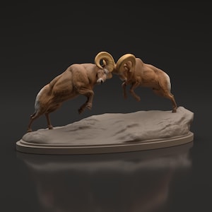 Puede incluir: Escultura que representa dos borregos cimarrones en una pose de choque de cabezas. Los carneros son marrones con marcas color crema y grandes cuernos dorados curvados. La escultura está montada sobre una base ovalada marrón claro, de unos 30 cm.