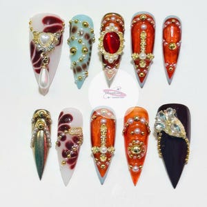 May include: Ten long, pointed, false fingernails with various designs.  The designs include a red heart with a pearl drop, a blue and gold animal print, a red jewel with a gold frame, a gold cross with pearls, a gold sword with pearls, a gold chain with pearls, a gold chain with rhinestones, a gold chain with pearls, a gold chain with pearls, and a black nail with a rhinestone design.
