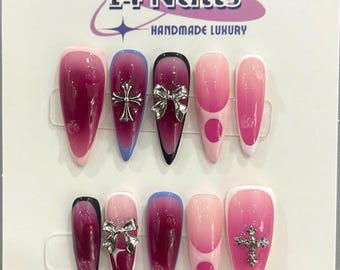 以下が含まれることがあります： ピンクとボルドーのグラデーションデザインの付け爪10本セット。一部の爪にはシルバーの十字架チャーム、一部にはシルバーのリボンチャーム、一部にはピンクのドットデザインが施されています。