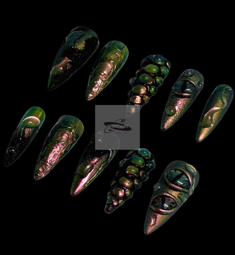 Peut inclure: Dix faux ongles iris&eacute;s et pointus. Les ongles pr&eacute;sentent divers motifs, notamment des textures et des d&eacute;tails en forme d'yeux. La palette de couleurs oscille entre le vert, le violet et l'or, sur fond noir.