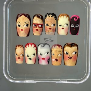 Puede incluir: Un conjunto de diez uñas postizas con diseños de rostros retro pintados a mano. Cada uña presenta rasgos faciales exagerados, como ojos grandes y labios rojos, con diferentes peinados. Se presentan en una caja de plástico transparente.