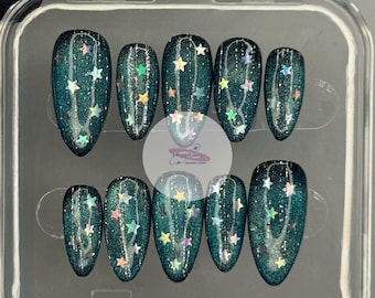 May include: A set of ten teal-colored, oval-shaped press-on nails. Each nail is decorated with iridescent star-shaped glitter. The nails are displayed in a clear plastic case.