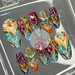 May include: A set of ten almond-shaped press-on nails. Each nail features a detailed design with floral and geometric patterns in shades of teal, orange, red, and gold. The nails are displayed in a clear plastic container.