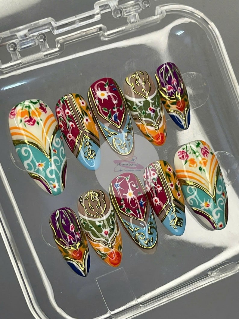 May include: A set of ten almond-shaped press-on nails. Each nail features a detailed design with floral and geometric patterns in shades of teal, orange, red, and gold. The nails are displayed in a clear plastic container.