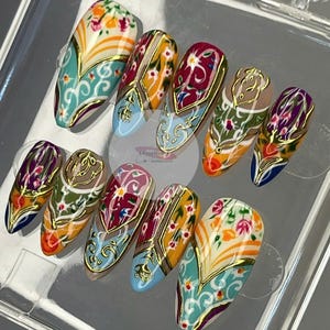 May include: A set of ten artificial nails with intricate designs. Each nail features a unique pattern with floral and geometric elements in shades of teal, orange, red, and gold. The nails are arranged in a clear plastic container.
