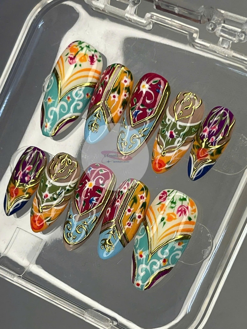 May include: A set of ten artificial nails with intricate designs. Each nail features a unique pattern with floral and geometric elements in shades of teal, orange, red, and gold. The nails are arranged in a clear plastic container.
