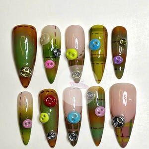 Może przedstawiać: Dziesięć długich, migdałowych sztucznych paznokci z zielonym, brązowym i kratkowym wzorem. Każdy paznokieć ma na górze guzik w innym kolorze.