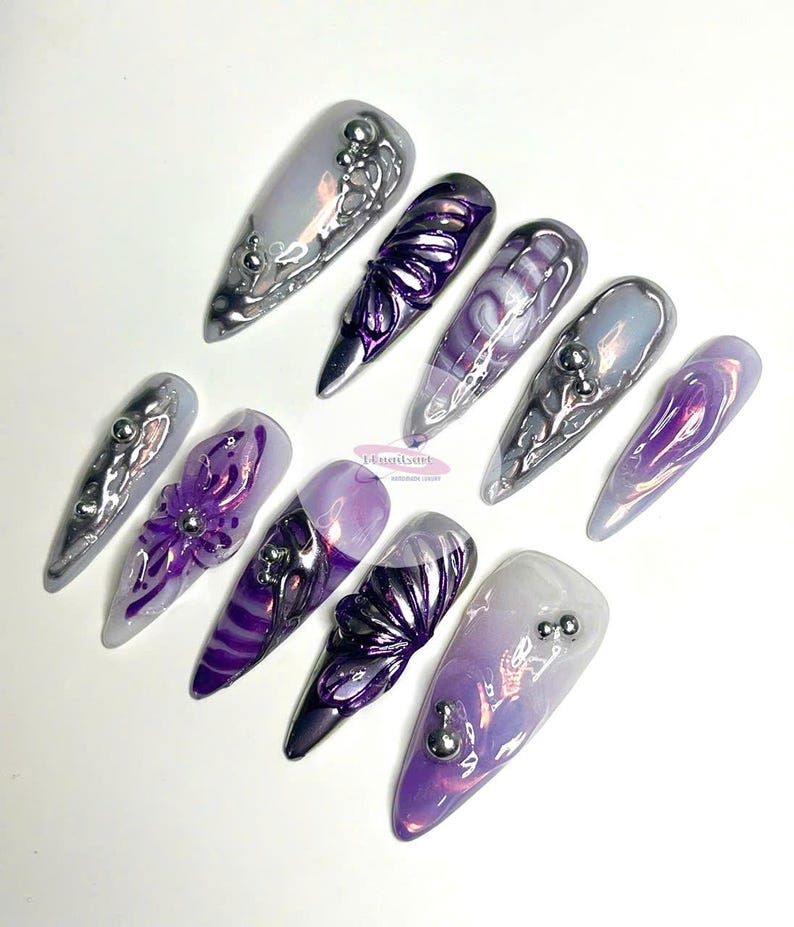 May include: Set of ten long, pointed, iridescent purple and silver press-on nails with various designs, including swirls, flowers, and abstract patterns.