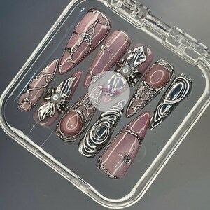 May include: A set of ten artificial nails in a clear plastic case. The nails are a mauve color with silver metallic embellishments. Some nails have a pearl accent. The nails are long and pointed.