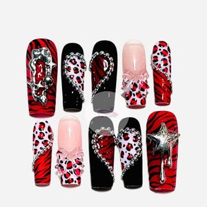 Puede incluir: Conjunto de diez uñas postizas con un diseño de cebra y leopardo rojo y negro. Algunas uñas tienen adornos de corazón, estrella y lazo plateados.