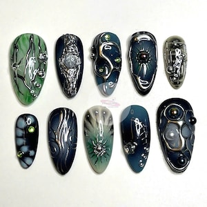May include: Ten long, oval-shaped artificial nails with intricate designs. Each nail features a different design with a combination of black, green, silver, and white colors. Some nails have a 3D effect with small beads and other embellishments.