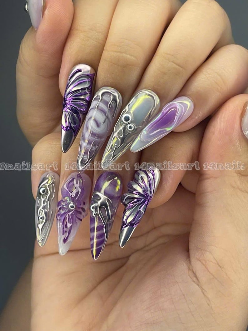 May include: Purple and silver butterfly nail art with a clear iridescent base. The nails are long and pointed.