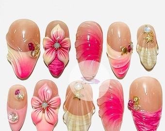 May include: A set of ten artificial nails with various designs. The nails feature a nude base with pink and white accents, including floral and seashell embellishments, and decorative gems.