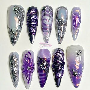 May include: Set of ten long, pointed, iridescent purple and silver nail tips with various designs, including butterflies, swirls, and flowers.