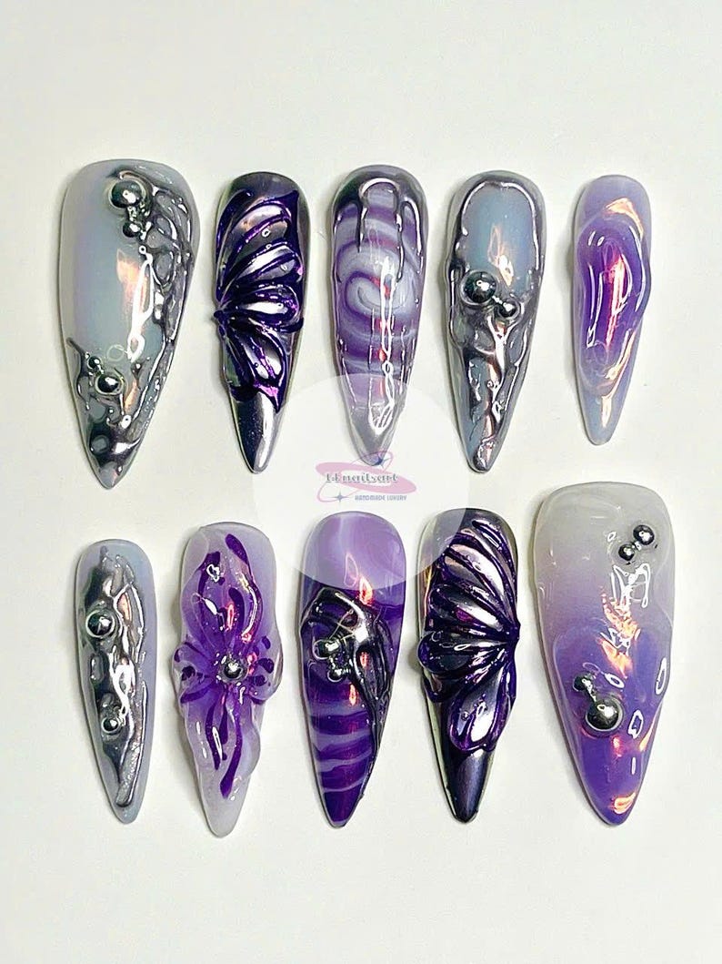 May include: Set of ten long, pointed, iridescent purple and silver nail tips with various designs, including butterflies, swirls, and flowers.
