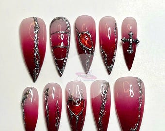 May include: Set of ten long, pointed, red and white ombre false nails with silver chain and heart designs. Some nails have a red heart or cross charm.