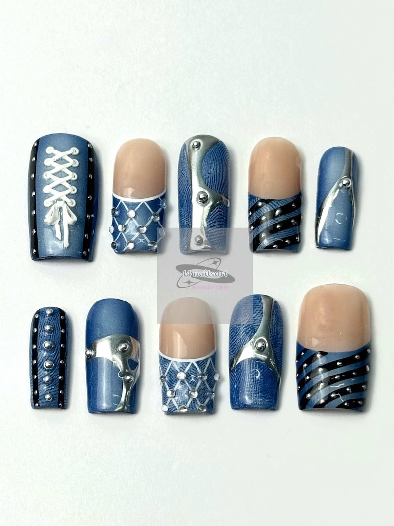 May include: A set of ten artificial nails with various designs. The nails feature a mix of blue denim, silver accents, and nude-colored tips. Some nails have a lace-up design, while others have silver embellishments or striped patterns.