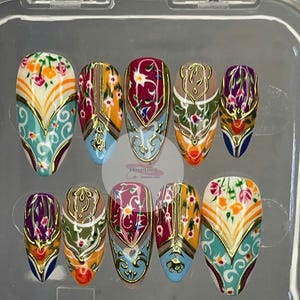 May include: A set of ten press-on nails with an ornate design. Each nail features a base color of white, blue, or tan, with floral and geometric patterns in shades of red, orange, and gold. The nails are in a clear plastic case.