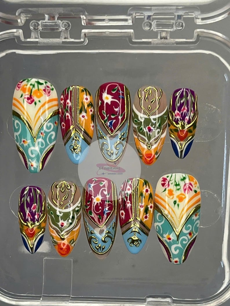 May include: A set of ten press-on nails with an ornate design. Each nail features a base color of white, blue, or tan, with floral and geometric patterns in shades of red, orange, and gold. The nails are in a clear plastic case.